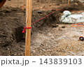 From a close viewpoint, a wooden stake is tied with a red measurement line marking the boundary at a construction site. 143839103