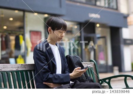 ベンチに座ってスマホを見る20代男性のビジネスマン ベンチに座ってスマホを見る20代男性のビジネスマン 143839846
