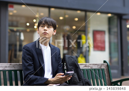 ベンチに座ってスマホを見る20代男性のビジネスマン ベンチに座ってスマホを見る20代男性のビジネスマン 143839848