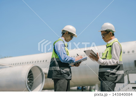 Team engineer in white hardhat standing and holding tablet working aircraft maintenance mechanics moving through hangar. 143840084