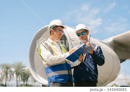 Team engineer in white hardhat standing and holding tablet working aircraft maintenance mechanics moving through hangar. 143840085