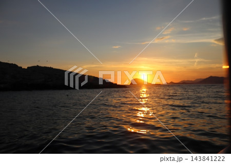 Sunset behind isolated rocky islet in Adriatic Sea with golden light on water 143841222