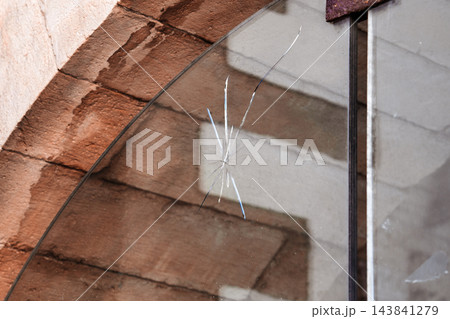 Crack and impact mark on a transparent glass window pane installed inside an old stone archway Crack and impact mark on a transparent glass window pane installed inside an old stone archway 143841279