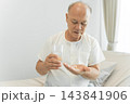 Senior man taking medication with water at home for health management 143841906