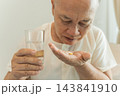 Senior man taking medication with a glass of water at home for health management. 143841910