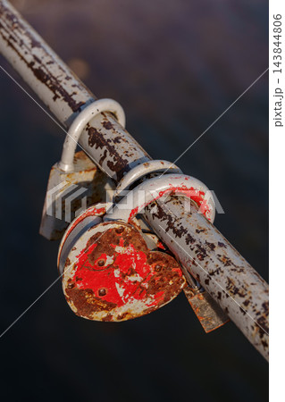 Old rusty red heart shaped padlock locked on metal railing. Nostalgia, passing time and relationship concept with dark background Old rusty red heart shaped padlock locked on metal railing. Nostalgia, passing time and relationship concept with dark background 143844806