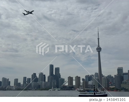 Toronto, Canada Airplane flying over Toronto skyline and ferry boat on water, cloudy sky and urban Toronto, Canada Airplane flying over Toronto skyline and ferry boat on water, cloudy sky and urban 143845101