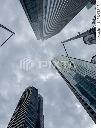 Skyscrapers viewed from below against a cloudy sky, showcasing modern architecture with glass Skyscrapers viewed from below against a cloudy sky, showcasing modern architecture with glass 143845243