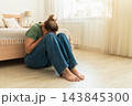 Woman sitting on bedroom floor, covering face and crying, illustrating concepts of sadness, depression, and loneliness at home 143845300