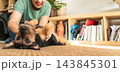 Woman playing with her pet dog on the carpet at home, enjoying a moment of companionship and happiness. Caring and loving pets. A happy moment in life 143845301