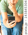 An adult woman focusing on phone screen, holding hand on chin, thinking about information or making a decision. Chatting, surfing social media, watching video content 143845304
