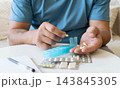 Man arranges capsules and pills into medication organizer. Organizing medication intake, adhering to treatment schedule, and maintaining daily wellness habits 143845305