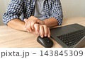 Close-up of man holding his wrist next to laptop and computer mouse. Carpal tunnel syndrome, repetitive strain injury (RSI), and wrist pain associated with computer work 143845309