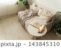 Cozy living room interior for relaxation. Sofa with throw blanket and pillows, coffee table, open book, lit candles. Concept of leisurely lifestyle, slow living 143845310