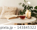 Warm atmosphere creating sense of coziness and relaxation, book, cup of tea, and lit candles on table. Concept of slow living, a mindful lifestyle, cozy home 143845322
