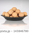 Front view of whole unshelled walnuts stacked in a black dish with reflection on white background 143846780