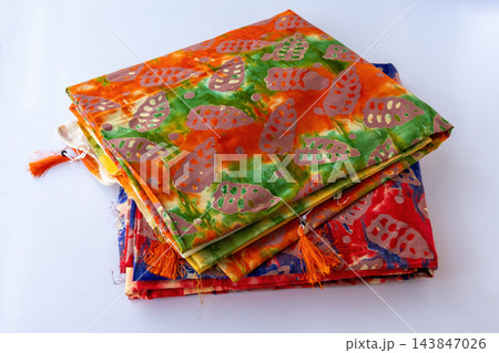 Folded colorful batik printed unstitched cotton three piece suit fabrics on white background. Traditional South Asian women clothing material. 143847026