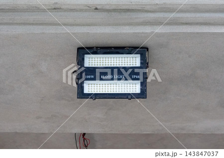 Outdoor 100W LED flood light mounted on a concrete wall structure. Waterproof IP66 security lamp used for architectural lighting. 143847037
