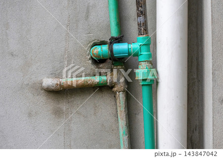 Green PPR plastic water pipes connected to a concrete wall outdoor structure. Plumbing installation and drainage pipeline for residential building. Green PPR plastic water pipes connected to a concrete wall outdoor structure. Plumbing installation and drainage pipeline for residential building. 143847042