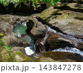 Water flowing between dark volcanic rocks forming natural pools and cascades viewed from above in tropical river 143847278