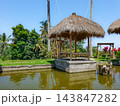 Traditional Balinese thatched roof gazebo on stone platform surrounded by calm pond with palm trees 143847282