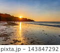 People Silhouetted on Tropical Beach at Golden Sunset with Sun Reflection on Wet Sand 143847292