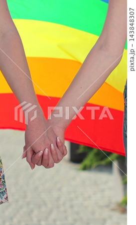 Vertical video. Young women walking on the street wrapped in rainbow flag, holding hands. Lesbian relationships, lgbt concept. 143848307