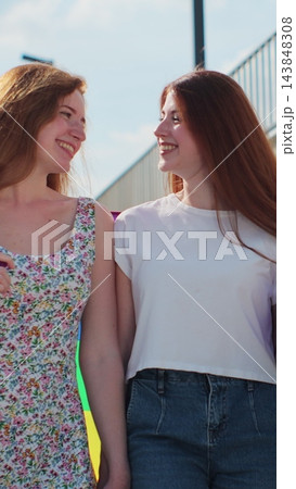 Vertical video. Young women walking on the street wrapped in rainbow flag, holding hands, smiling. Lesbian relationships, lgbt concept. 143848308