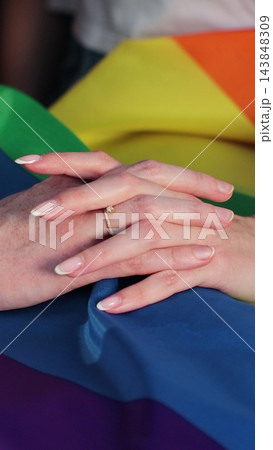 Vertical video. Close up lesbian couple in love holding hands on rainbow flag. Lgbt family holding hands outside. Woman relationship, lgbt family concept. Vertical video. Close up lesbian couple in love holding hands on rainbow flag. Lgbt family holding hands outside. Woman relationship, lgbt family concept. 143848309