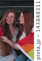 Vertical video. Young lesbian couple taking selfie and sit in the back of the car. Two happy girlfriends pose with rainbow flag. Lgbt woman, showing love to. 143848311