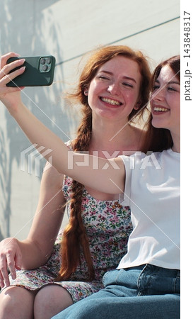Vertical video. Young adult lesbian couple taking selfie in the city. Two happy girlfriends pose with rainbow flag. Lgbt woman, showing love to each other. 143848317