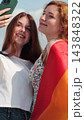 Vertical video. Young lesbian couple taking selfie in the city. Two happy girlfriends pose with rainbow flag. Lgbt woman, showing love to each other. 143848322