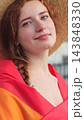 Vertical video. Portrait of young woman in a hat with long red hair covering herself in lgbt flag while looking at camera. 143848330