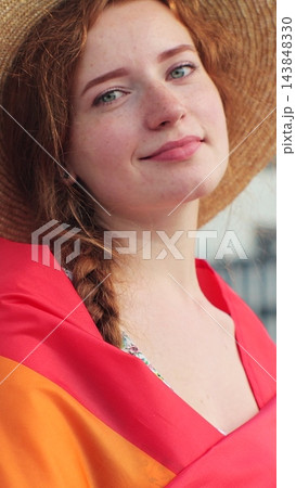 Vertical video. Portrait of young woman in a hat with long red hair covering herself in lgbt flag while looking at camera. Vertical video. Portrait of young woman in a hat with long red hair covering herself in lgbt flag while looking at camera. 143848330