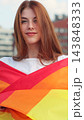 Vertical video. Portrait of a young woman with long red hair covering herself in lgbt flag while looking to camera. 143848333