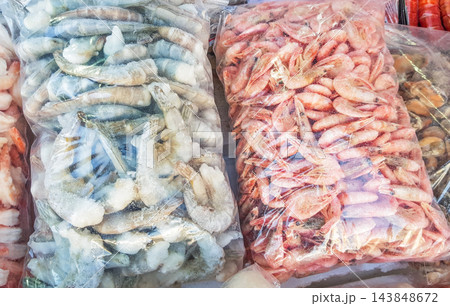 Two large plastic bags of frozen raw and cooked shrimp, on the counter of the fish market 143848672