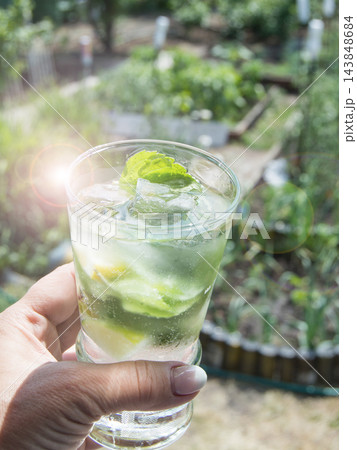 A refreshing mojito drink in a woman's hand. Vertical, outdoors, on a sunny summer day 143848684