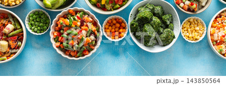 Freshly frozen vegetables in vibrant colors, neatly organized on plates with a soft blue backdrop, offering a glimpse into winter food preparation and storage, banner Freshly frozen vegetables in vibrant colors, neatly organized on plates with a soft blue backdrop, offering a glimpse into winter food preparation and storage, banner 143850564