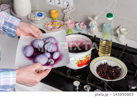 Hands hold eggs dyed with dried hibiscus Sudanese rose over a stove, with hibiscus in a bowl and dye in a pot after seven minutes for Easter Hands hold eggs dyed with dried hibiscus Sudanese rose over a stove, with hibiscus in a bowl and dye in a pot after seven minutes for Easter 143850803