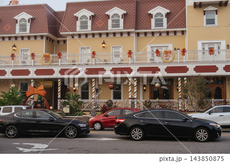 A large yellow Victorian hotel is decorated with wreaths, bows, ornaments, lights, and a giant ribbon. Several cars are parked along the street in front of the festive building. A large yellow Victorian hotel is decorated with wreaths, bows, ornaments, lights, and a giant ribbon. Several cars are parked along the street in front of the festive building. 143850875