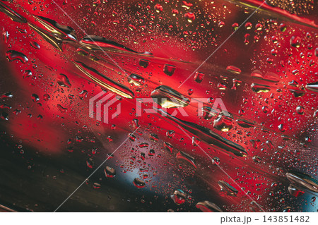 Water droplets on glass with intense red neon lighting reflection. Macro photograph of clear water drops condensed on glass surface with a dramatic deep red and dark neon glow background texture 143851482