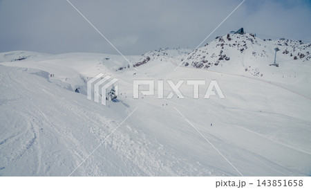Snow-covered mountain slope with skiers near rocky peak under overcast sky, Caucasus Elbrus region Snow-covered mountain slope with skiers near rocky peak under overcast sky, Caucasus Elbrus region 143851658