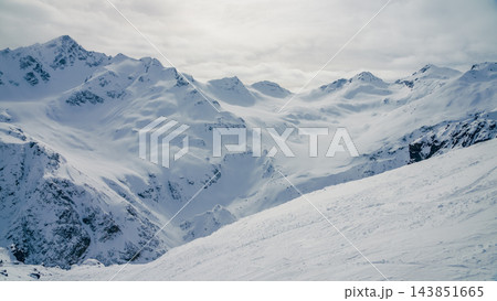 Expansive snow-covered Caucasus mountain range with sunlit ridges and broad winter valley view Expansive snow-covered Caucasus mountain range with sunlit ridges and broad winter valley view 143851665