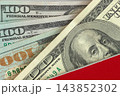 Close-up of hundred US dollar bills showing Benjamin Franklin portrait. Macro view of several hundred US dollar banknotes lying under red background of book cover 143852302