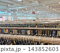 Clothing racks with hangers in retail store, blurred background. Close-up view of metal clothing rails filled with clothes hangers, large brightly lit fashion shop with bokeh bokeh light background 143852603