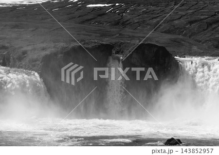 Godafoss waterfall in monochrome with surging water, dark rocks and drifting spray 143852957