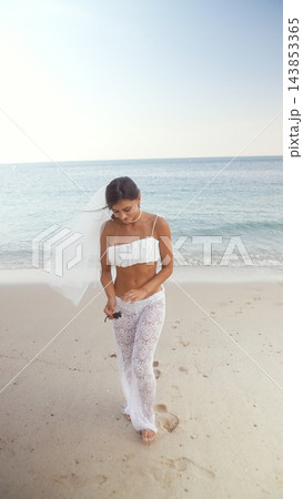 Bride looking down while walking barefoot on a sandy beach Bride looking down while walking barefoot on a sandy beach 143853365