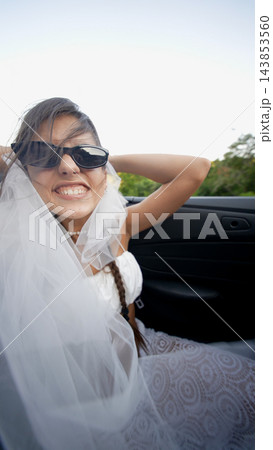 Bride in sunglasses smiling from a car passenger seat 143853560