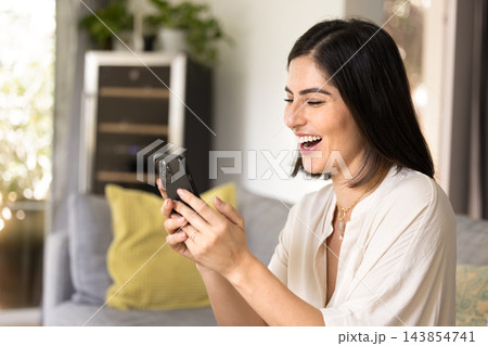 Laughing woman reading incredible news on smartphone at home Laughing woman reading incredible news on smartphone at home 143854741