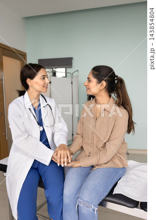 Positive Middle Eastern doctor holding hands of young Indian patient Positive Middle Eastern doctor holding hands of young Indian patient 143854804
